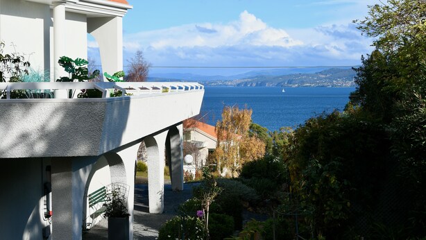 Un edificio costero con balcón que da al mar, mostrando una vista de la costa y un puente a lo lejos.