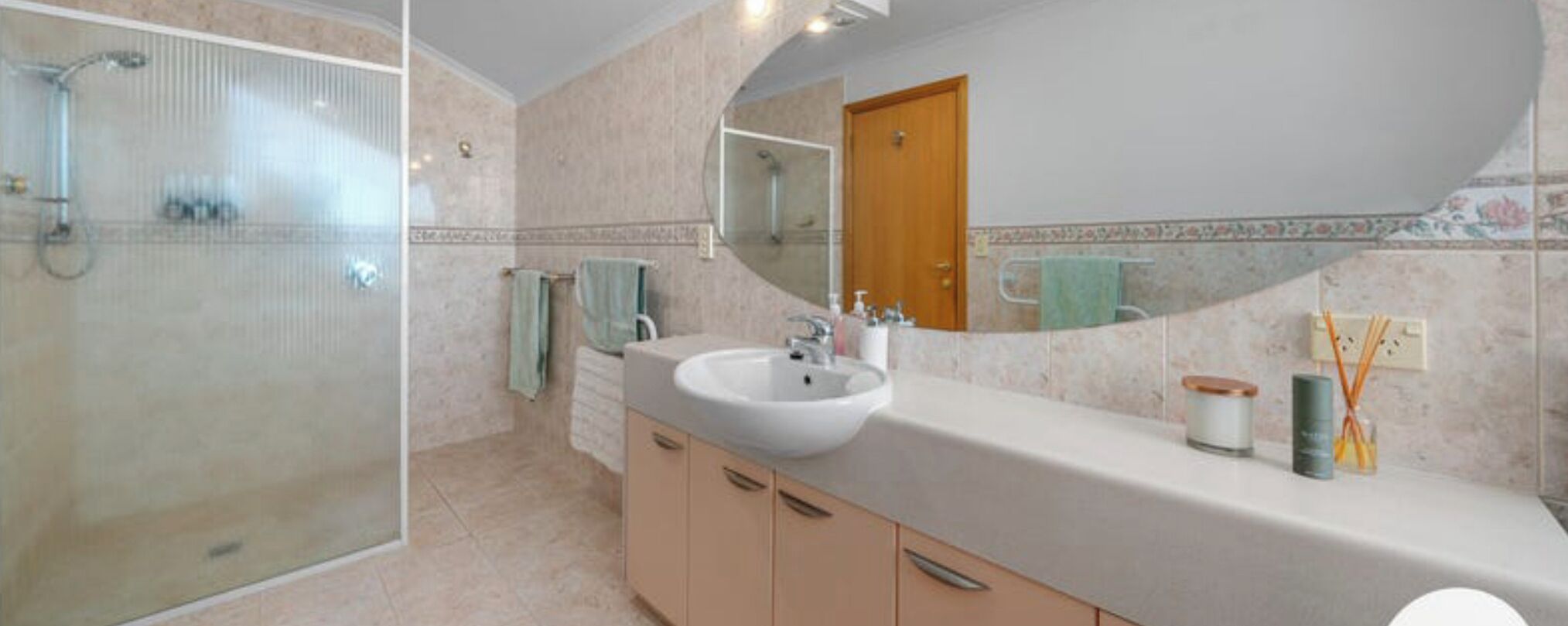A bathroom with a glass shower enclosure, a sink with a mirror above it, and a wooden door.