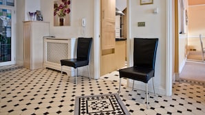 Een hotelkamer met een geruite vloer, twee zwarte stoelen, een radiator, een telefoon en een schilderij van bloemen.