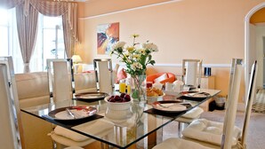 Een eetruimte met een glazen tafel, witte stoelen, een kroonluchter en een bloemenvaas.