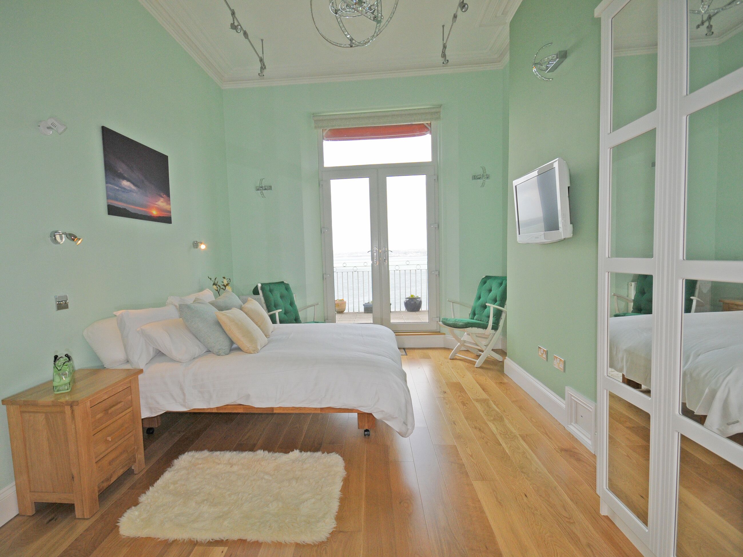 A bedroom with two beds, a wooden dresser, a fluffy rug, a green chair, and a TV on the wall.