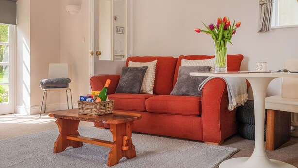 A living room with a red sofa, a wooden coffee table, a white side table, and a vase with flowers.