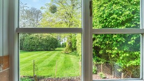 A window with a view of a well-maintained garden, including a lawn and various trees.