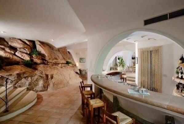 A modern interior with a stone wall, a curved seating area, and a bar. - A Vacation on the Emerald Coast in Cala di Volpe (loc. cala di volpe)