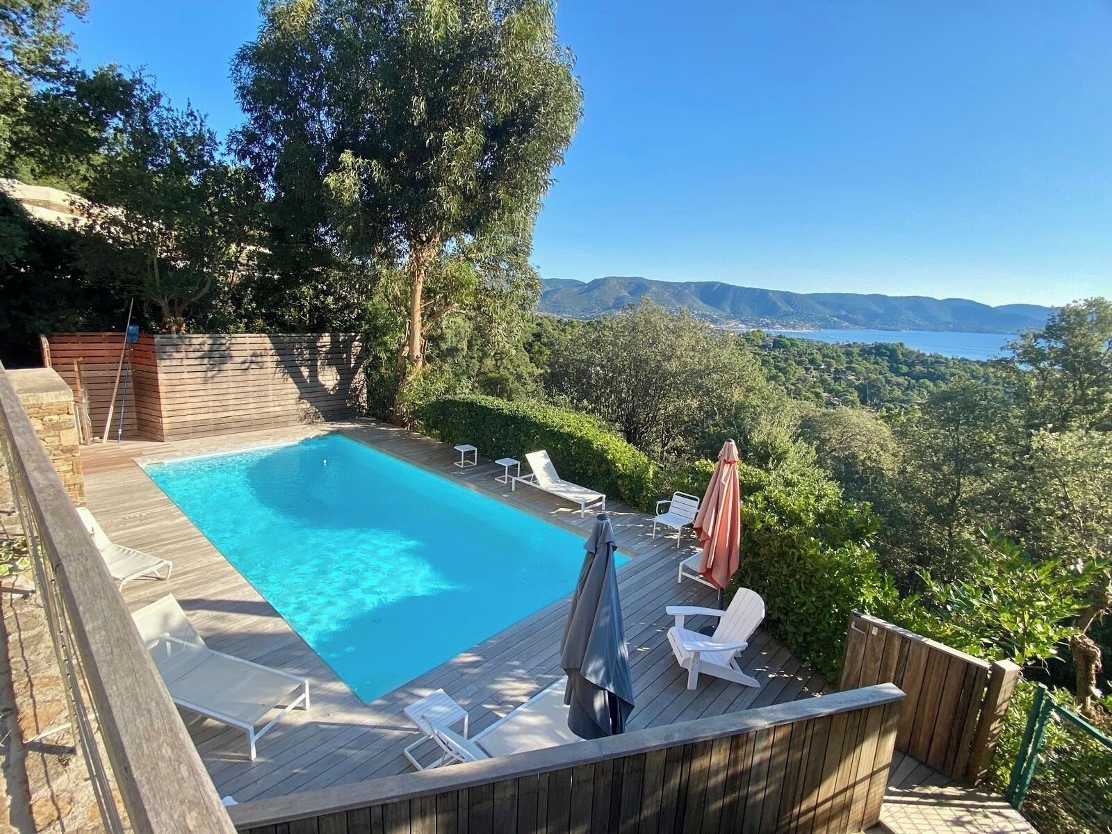 Un terrazzo in legno con piscina, poltrone da relax bianche e vista su un paesaggio montuoso.