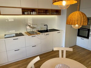 Une cuisine moderne avec des meubles blancs, un évier noir, un four encastré et un plan de travail en bois.