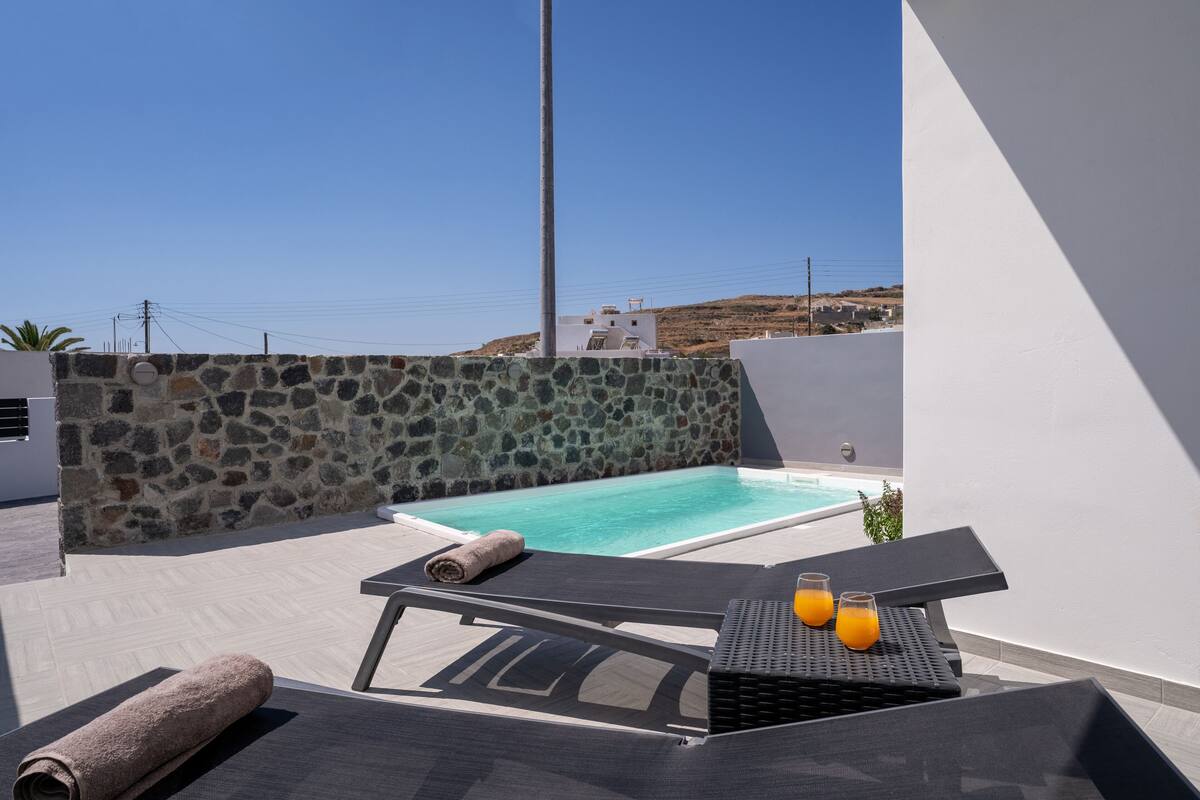 Uma área de piscina no terraço, com paredes de pedra, espreguiçadeiras e uma mesa com bebidas.
