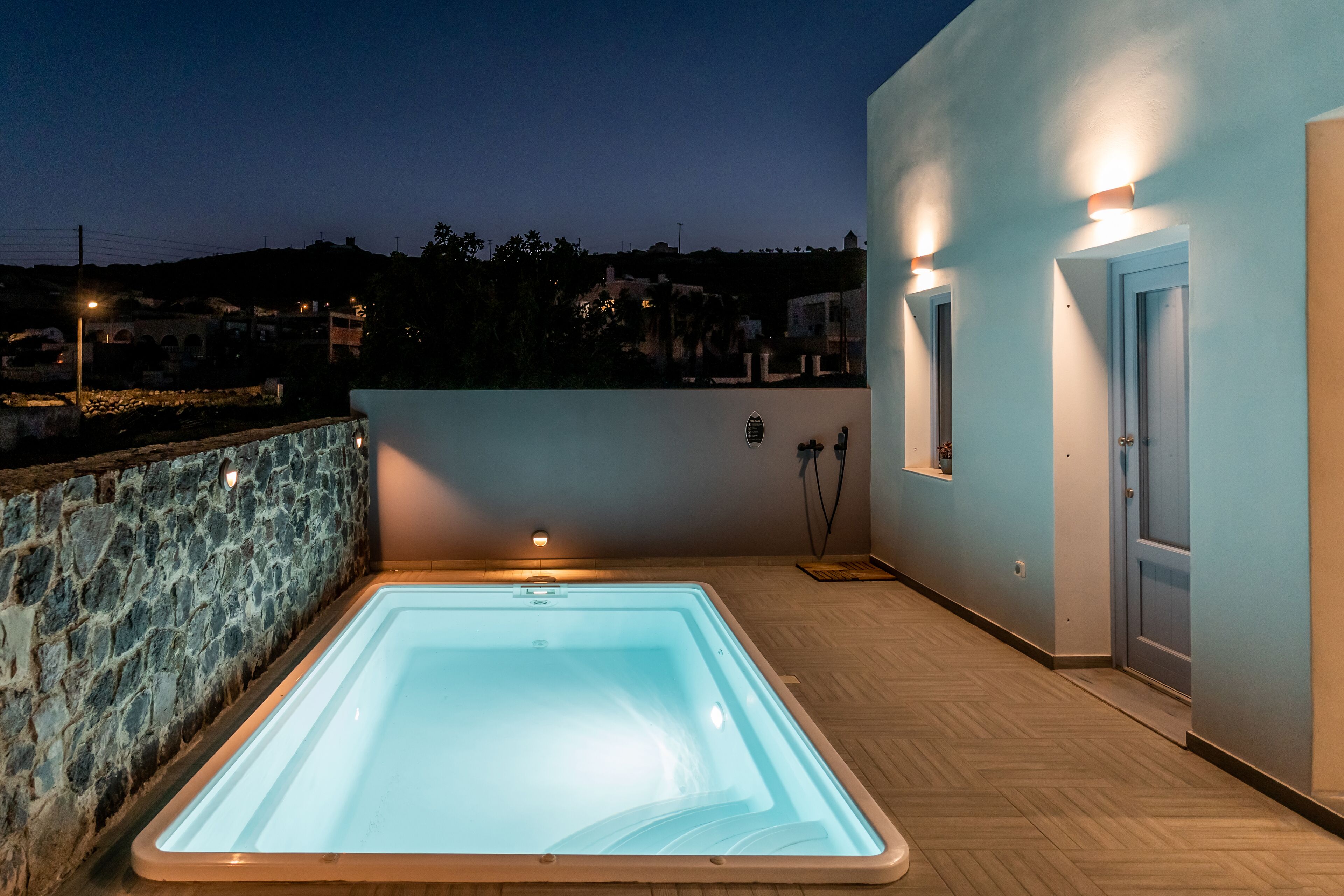 Ein rechteckiger Pool mit einer Steinmauer an einer Seite, einem Holzboden und einer hellblauen Wand mit einer Tür und einer Leuchte.