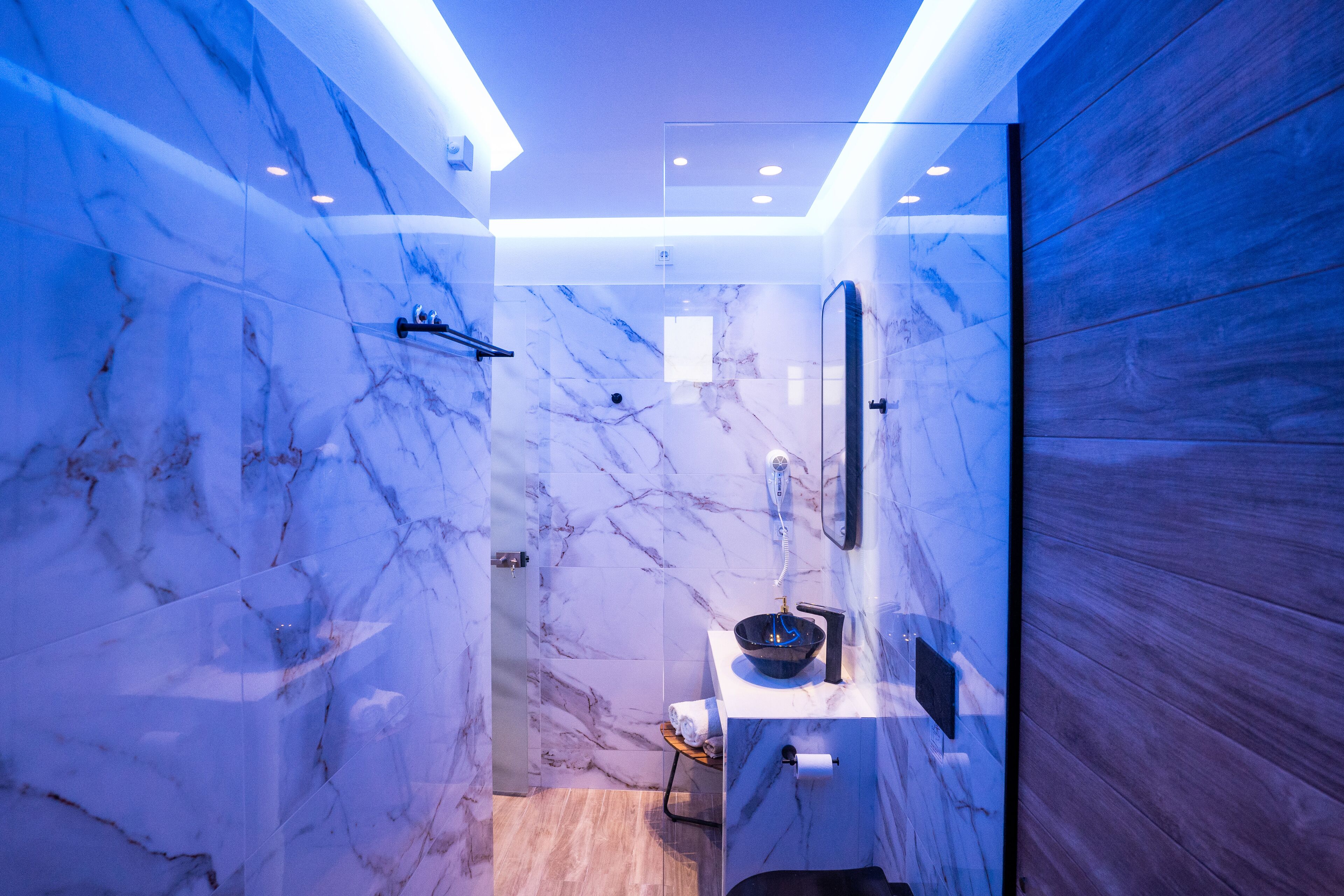Een moderne badkamer met marmeren wanden, een glazen douchecabine en een houten paneel als accent.