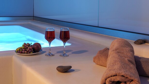 Zona de spa con un jacuzzi, dos copas de vino tinto, un bol de fruta y toallas.