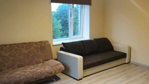 A living room with a brown patterned sofa, a white sofa, and a window with a view of trees.