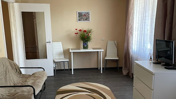 A compact living space with a sofa, a small table with a vase of flowers, a television, and a bed.