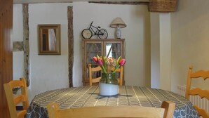 A dining area with a round table, chairs, a vase with flowers, a clock, a lamp, and a wicker basket on the wall. - Jasmine Cottage - UK4176 (Middle Mayfield, near Ashbourne)