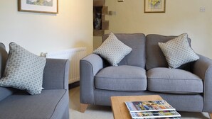 A living room with two grey sofas, patterned cushions, a coffee table with magazines, and framed floral artwork on the walls. - Jasmine Cottage - UK4176 (Middle Mayfield, near Ashbourne)