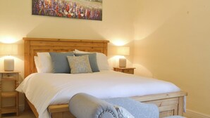 A bedroom with a wooden headboard, a large bed with white bedding, two bedside lamps, a wooden nightstand, and a blue upholstered chair. - Jasmine Cottage - UK4176 (Middle Mayfield, near Ashbourne)