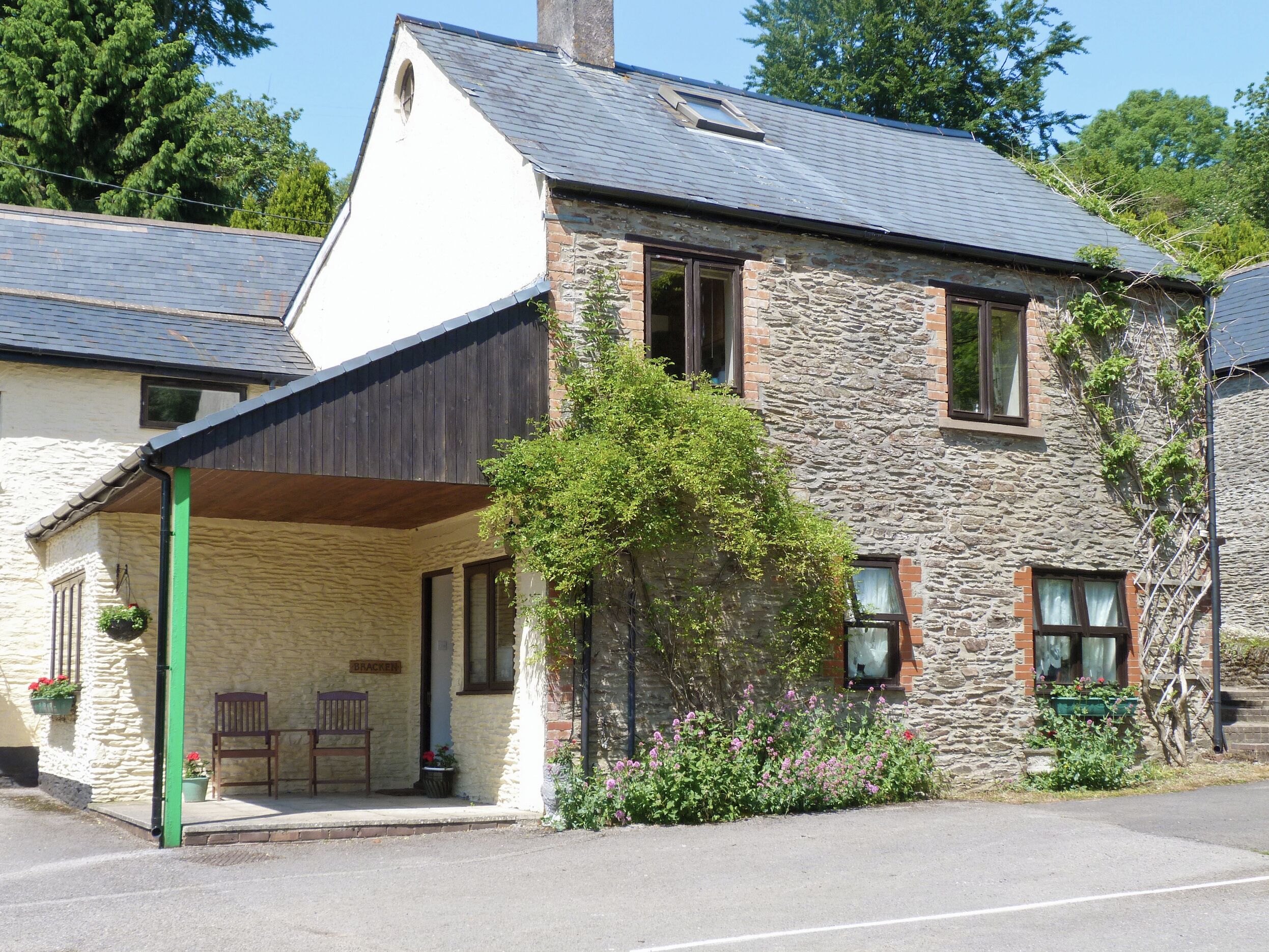 Un bâtiment en pierre avec un porche couvert, une enseigne indiquant « BRACKER » et une chaise verte à l’extérieur.