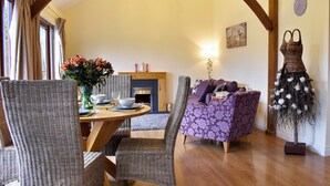 A cozy living room with a wooden dining table, wicker chairs, a purple sofa, and a fireplace.