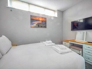 Una habitación de hotel con cama, un cuadro de un atardecer, televisión y un escritorio con espejo.