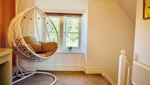 Una habitación con una mecedora, un ventanal con vistas a follaje y un radiador.