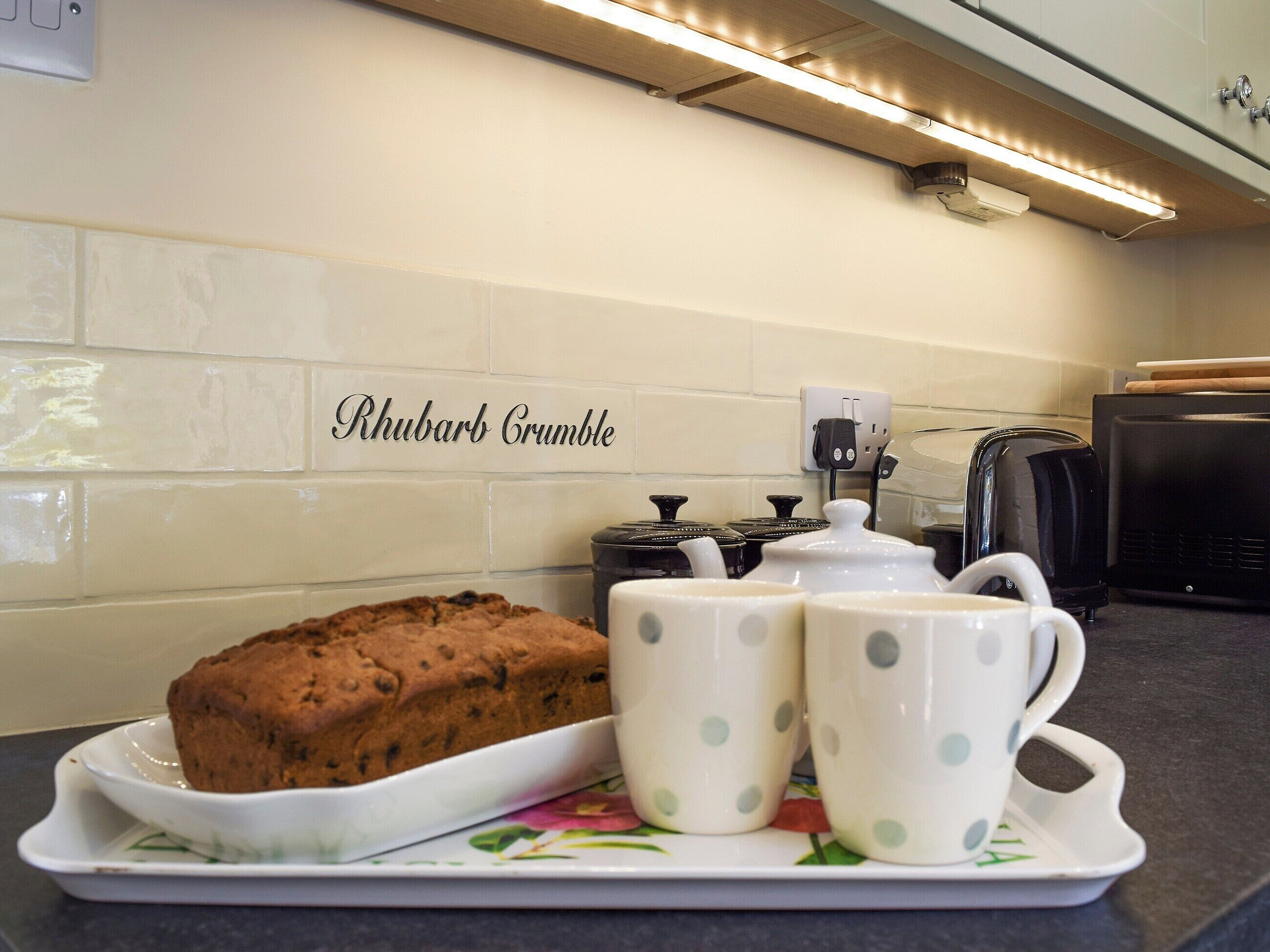A kitchen with a loaf of bread, two teacups, and a teapot on a tray.
