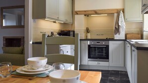 Una cocina moderna con armarios blancos, horno empotrado y comedor con una mesa dispuesta para dos personas.