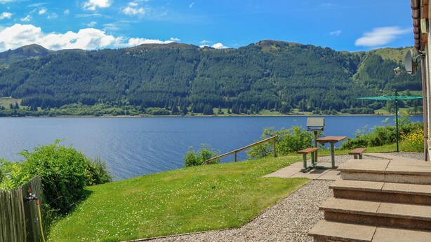 A lakeside view with a wooden deck, steps leading to a bench, and a mountain in the background. - 2 bedroom accommodation in by Inverinate, Kyle (by Inverinate, Kyle)