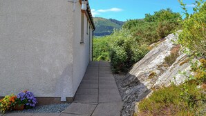 A narrow pathway leading to a building with a white exterior and a brown roof. - 2 bedroom accommodation in by Inverinate, Kyle (by Inverinate, Kyle)