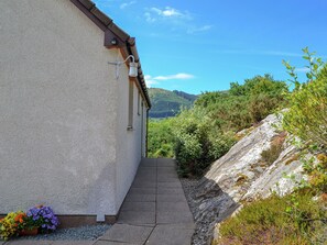 A narrow pathway leading to a building with a white exterior and a brown roof.
