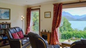 A living room with a view of a lake and mountains, a fireplace, a bookshelf, and leather furniture. - 2 bedroom accommodation in by Inverinate, Kyle (by Inverinate, Kyle)