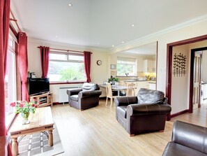 A living room with a television, two sofas, a dining table with chairs, a kitchen area, and a view of greenery outside. - 2 bedroom accommodation in by Inverinate, Kyle (by Inverinate, Kyle)