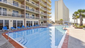 A hotel with a swimming pool, blue lounge chairs, and a multi-story building with balconies.