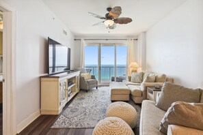 A living room with a flat-screen TV, a ceiling fan, a sofa set, and a view of the ocean through large windows. - Sunrise Beach Resort by Book That Condo (Panama City Beach)