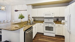 A modern kitchen with white cabinetry, granite countertops, a built-in oven, and a microwave.