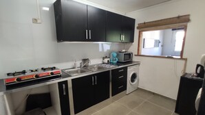 A compact kitchen with black cabinets, a gas stove, a microwave, a coffee maker, and a washing machine. - Seasonal Rental, Duplex (Saint-Denis)