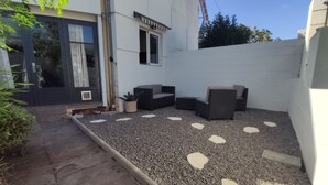 A patio area with a gravel floor, outdoor seating, and a white wall. - Seasonal Rental, Duplex (Saint-Denis)