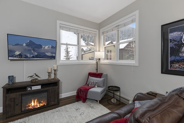 A living room with a fireplace, a mounted TV, and a large window with a view of mountains.
