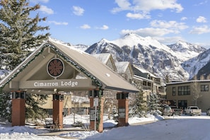 A lodge with a snow-covered mountain backdrop, a covered entrance, and a sign indicating amenities like a gift shop and lift tickets.