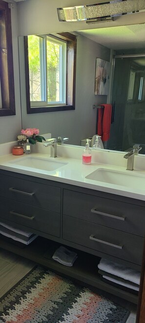 Un baño con dos lavamanos, un espejo grande y una ventana. Hay toallas y un florero con flores en la encimera.