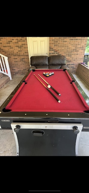 Ein Billardtisch mit roter Spielfläche, zwei braune Billardstöcke und ein Satz Billardkugeln.