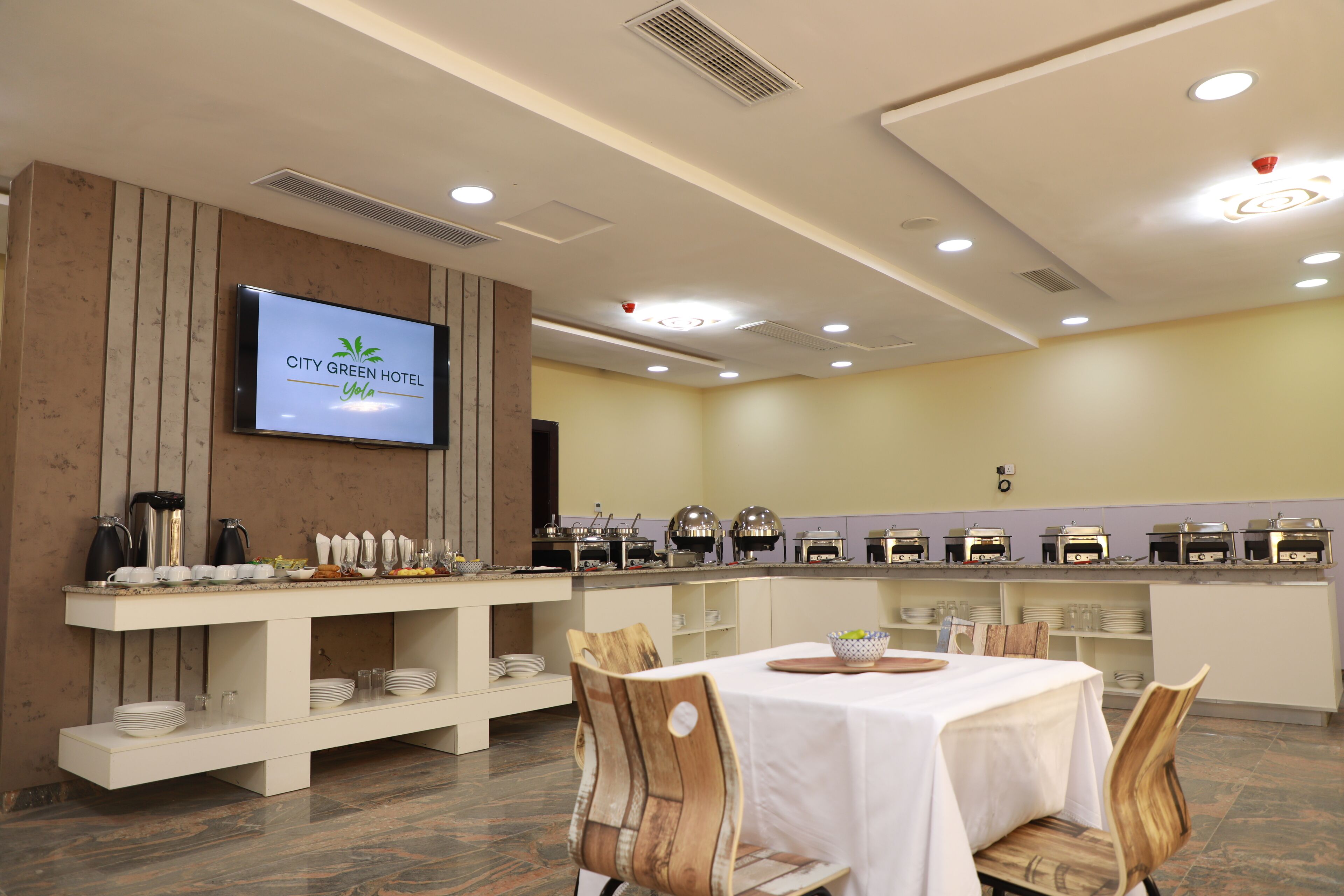Uma área de refeições de hotel com serviço de buffet, uma televisão exibindo o nome do hotel e um interior limpo e moderno.