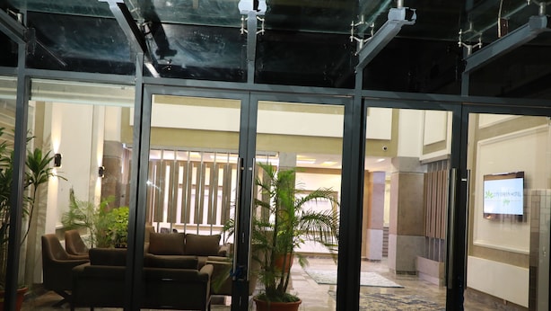 A lobby with glass doors, a sofa, and potted plants. - City Green Hotel Yola (Jimeta)