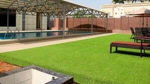 A swimming pool with a covered area, artificial grass, and outdoor furniture. - City Green Hotel Yola (Jimeta)