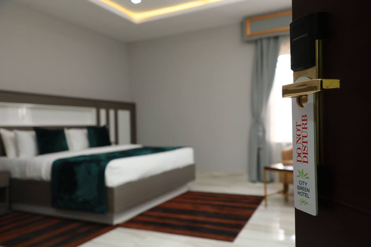 Una habitación de hotel con cama, mesita de noche, silla y una puerta con un cartel.