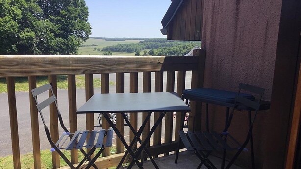 A small outdoor patio with a table and chairs, overlooking a scenic landscape. - APPARTEMENT VACANCES LAGUIOLE (Laguiole)