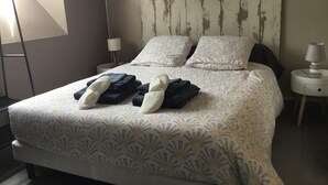 A neatly made bed with a patterned bedspread, two pillows, and folded towels. There is a bedside lamp on a nightstand beside the bed. - APPARTEMENT VACANCES LAGUIOLE (Laguiole)