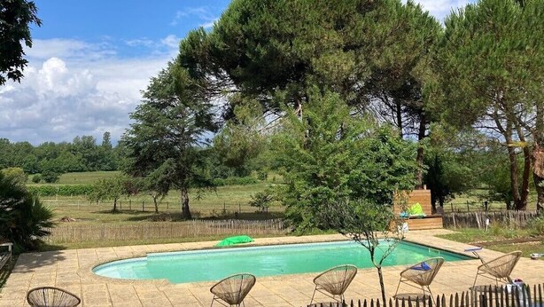 Piscina com deck de madeira, cercada por árvores e um muro de madeira.