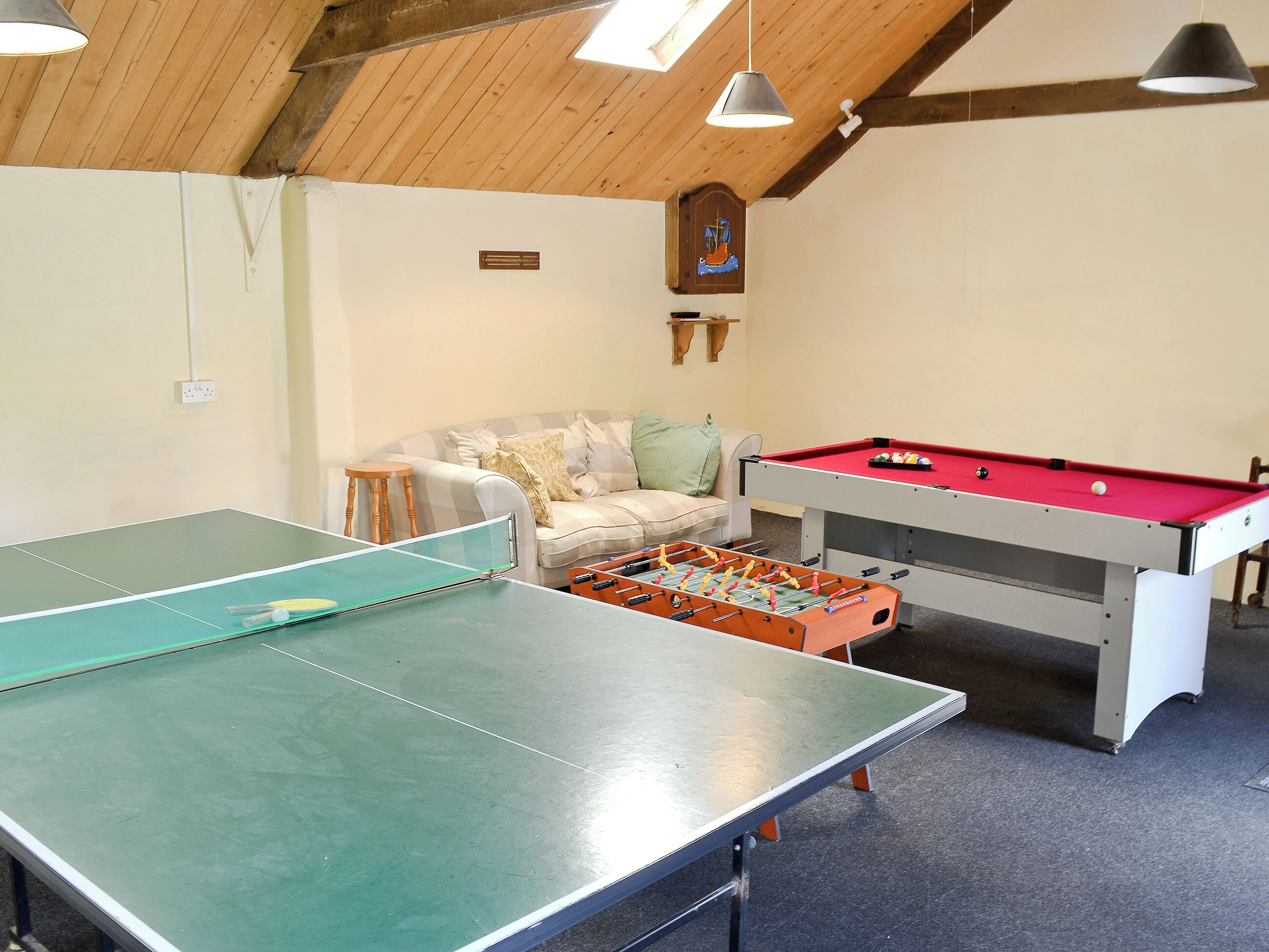 A room with a ping pong table, a foosball table, and a pool table.