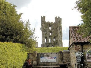 Ruinas de un castillo histórico con un cartel que indica un estacionamiento y mercado cerca.