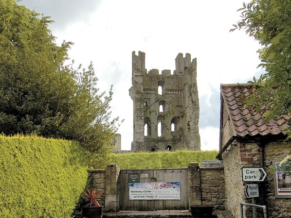 Ruínas de um castelo histórico com uma placa indicando um estacionamento e um mercado por perto.