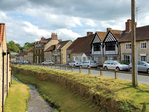 A row of traditional stone houses with timber framing, a paved street, and parked cars. - Spacious lodge in peaceful countryside, enjoying lovely views. (Nawton, near Helmsley)